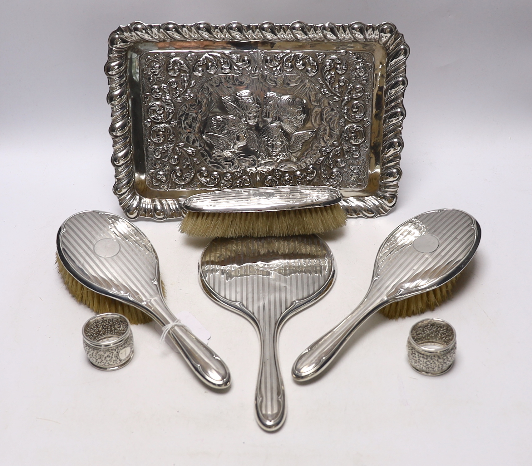 An Edwardian repousse silver dressing table tray, with Reynold's Angels decoration, Birmingham, 1904, 29.7cm, a silver dressing table mirror, two brushes, a clothes brush and two napkin rings.